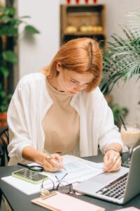 Une femme analysant des documents financiers à l'aide d'un ordinateur portable et d'une calculatrice à l'intérieur.