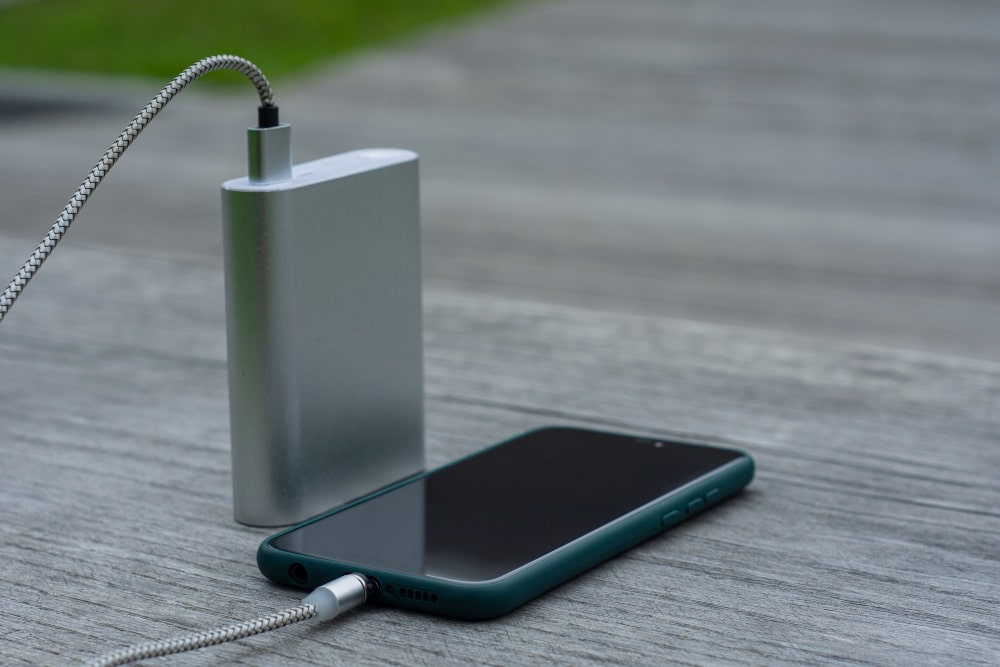 Une batterie externe argentée recharge un smartphone posé sur une table en bois